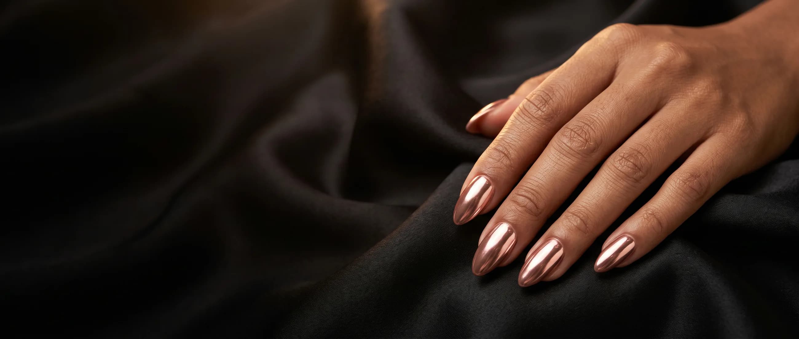 Main aux ongles chrome rose gold posée sur un satin noir